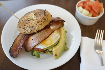 Bacon egg avocado lettuce on a toasted bagel and fruit salad