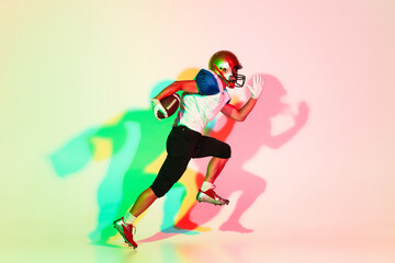 Fototapeta na wymiar American football player isolated on gradient studio background in neon light with shadows. Professional sportsman during game playing in action and motion. Concept of sport, movement, achievements.