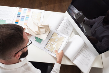 Approval of the construction project. A man sits at a Desk with a house plan, drawings, and color...