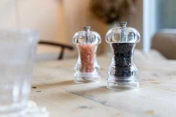 The black pepper and Himalayan salt grinder put on a wooden table with a glass of water in the front.