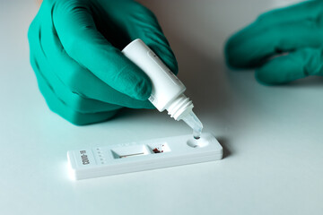 Doctor hands in green latex gloves performing covid-19 rapid test on white table