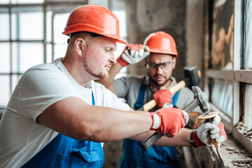 Builders at a large construction site removing plaster from an old brick wall near the window