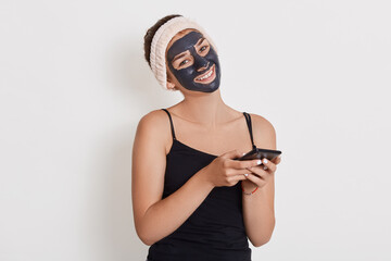 Beautiful smiling girl with black mask on her face, holding smart phone in hands, close up portrait...