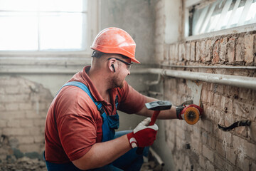 Highly skilled worker in a safety helmet, handling a brick wall on a large construction site