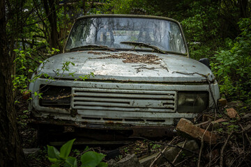 Obraz na płótnie Canvas An abandoned car standing in a forest parking lot among other abandoned vehicles