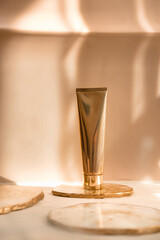 Golden cosmetic tube light pastel color background, lights and shadows. Natural minimalism look, clean sustainable concept. Minimal styling, still life. Beauty blogging, branding layout,  skin care ad