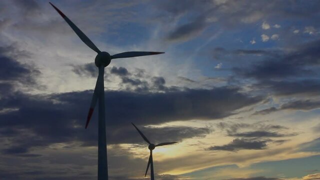 Holic turbines spinning in the wind at sunset, with sky with clouds, medium shot
