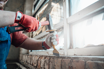 Builder's gloved hands working with hammer and chisel at the construction site