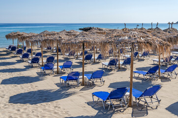Fototapeta na wymiar Straw beach umbrellas and sun chairs on the east coast of Zakynthos island in Greece