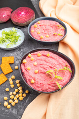 Hummus with beet and microgreen basil sprouts in ceramic bowl on a black concrete background. Side view, close up.