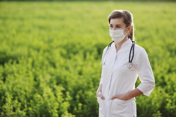 Female doctor or nurse wearing protective mask on green grass background