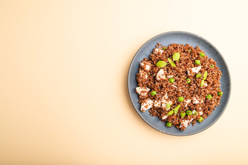 Quinoa porridge with green pea and chicken on ceramic plate on a pastel orange background. Top view, copy space.
