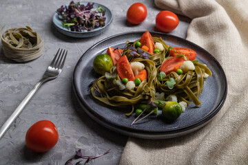 Tagliatelle green spinach pasta with tomato, pea and microgreen sprouts on a gray concrete background. Side view, close up.