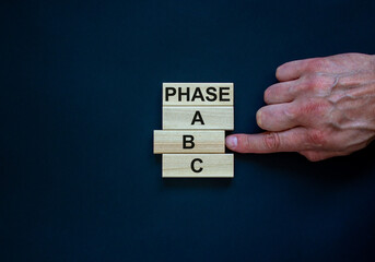 Wooden blocks form the words 'phase, A, B, C' on black background. Male hand. Beautiful background. Business concept, copy space.