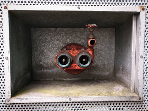 Fire extinguisher heads with water valve mounted inside box in the wall that looks like scuba diver's head or cute monster. Accidental art.
