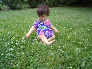 Little girl sitting in grass playing with clover