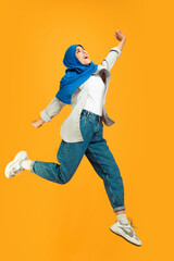 Jumping high emotional. Young muslim woman in casual on yellow studio background. Stylish, trendy. Beautiful brunette. Human emotions, facial expression, sales, ad, shopping concept. Copyspace.