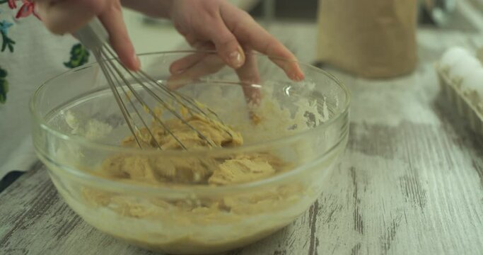 Female hands mixing creamy ingredients in a glass bowl by wire whisk. Close up