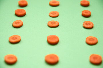 Flat lay composition with sliced carrot on green color background. Pattern. Top view, close up. Selective focus..