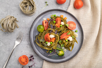 Tagliatelle green spinach pasta with tomato, pea and microgreen sprouts on a gray concrete background. Top view, close up.