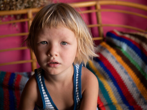 Portrait of funny child sitting on sofa covered with striped blanket