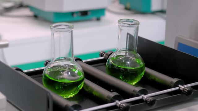 Chemistry, pharmaceutical, laboratory equipment concept. Slow motion: orbital shaker for mixing, shaking, blending biological samples in glass vials at pharmacy factory, medical exhibition: close up