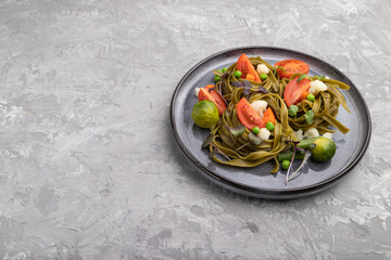 Tagliatelle green spinach pasta with tomato, pea and microgreen sprouts on a gray concrete background. Side view, copy space.
