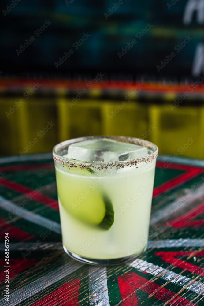 Wall mural A cocktail in a rocks lowball glass with a big ice cube, garnished with cucumber slice, spicy rim on the glass