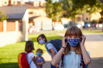 Child with face mask going back to school after covid-19 quarantine. Blonde girl putting on her face mask