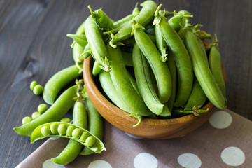 Pods of young green peas in a wooden bowl on a dark background. Green pea. Local products consumption concept. Farm products. Selective focus.