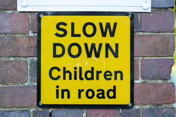 Naklejka premium a yellow sign on a brick wall outside a school stating slow down children in road