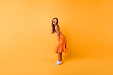 Fototapeta na wymiar Full-length portrait of gorgeous curly girl in orange skirt. Studio photo of positive lady dancing on yellow background.