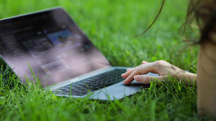 Image of girls hands typing. Freelance, work outside on a sunny day on a green lawn in the park. 