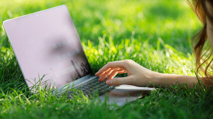 Image of girls hands typing. Freelance, work outside on a sunny day on a green lawn in the park. Selective focus