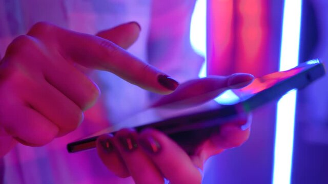 Woman using smartphone device at interactive exhibition or museum with purple illumination - scrolling and touching - close up view. Futuristic, retrowave, immersive, entertainment concept