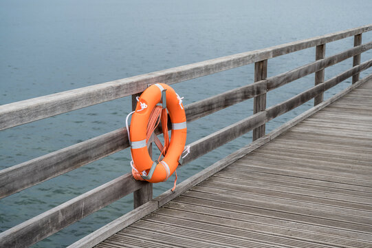 Hölzerner Steg an einem Hafen mit orangem Rettungsring für Notfälle
