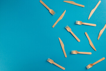 Wooden eco friendly disposable forks and knives arranged on blue background with copy space
