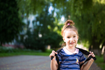 A little girl of Caucasian appearance in a school uniform with a backpack looks into the frame. Concept back to school. Elementary school, developing activities for preschoolers. Space for text