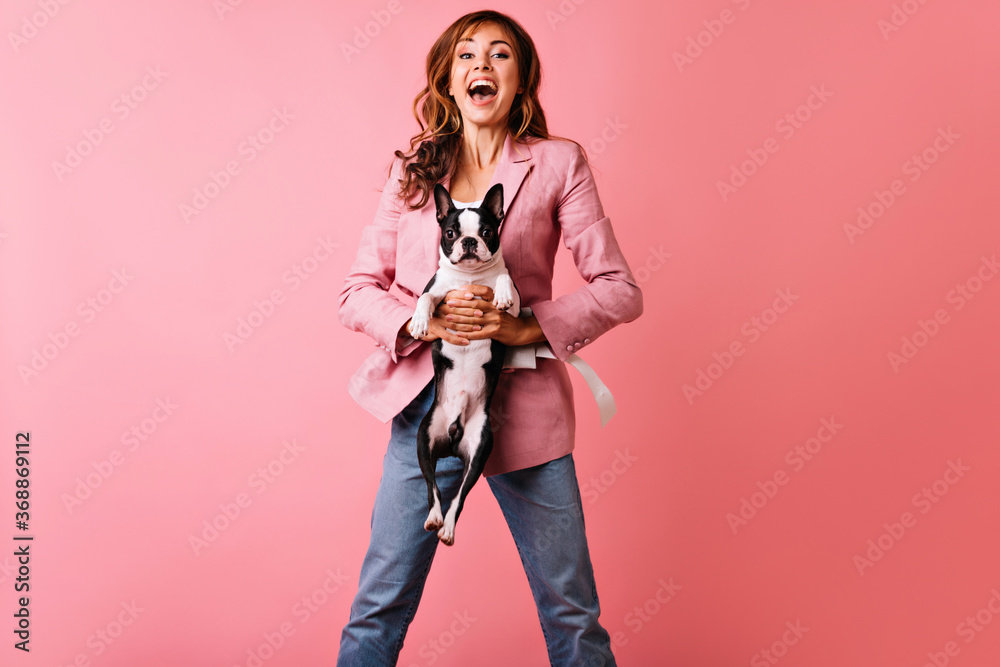 Wall mural Enchanting woman in casual outfit posing with dog. Indoor portrait of pretty ginger girl having fun in studio with french bulldog.