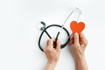 Elderly wrinkled hands holds a stethoscope and heart symbol. Heart care in old age concept.