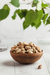Pistachios in a bowl on a light wooden table with green leaves in the background. Healthy snacks, healthy food. Nuts.