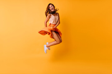 Full-length photo of tanned ginger girl jumping on yellow background and smiling. Adorable young...