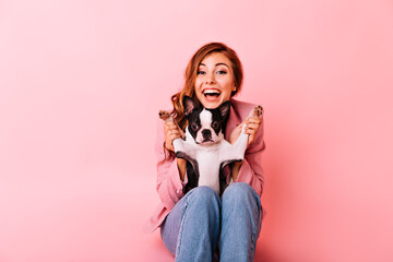 Obraz na płótnie Canvas Glad girl in jeans playing with funny little dog. Indoor portrait of excited ginger lady with curly hairstyle spending time with her puppy.