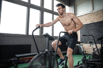 Fototapeta na wymiar Man using exercise bike at the gym. Fitness male using air bike for cardio workout at Functional training gym.