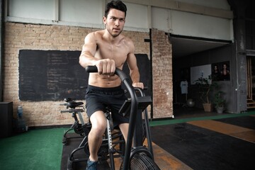 Obraz premium Man using exercise bike at the gym. Fitness male using air bike for cardio workout at Functional training gym.