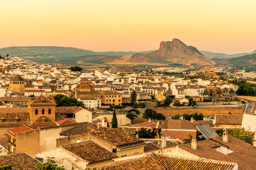 Obraz premium A view across the rooftops of Antequera, Spain toward the face-shaped mountain in the distance at sunset on a summers evening