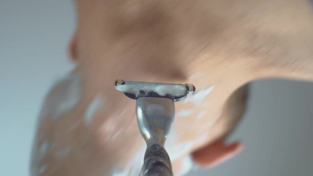 A man shaves his beard with a razor and shaving cream-close-up. A first-person camera attached to a shaving machine.