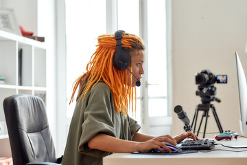 Love the Game. Female esport gamer, woman in headphones looking focused, playing online video game on PC while recording, filming vlog in the daytime © Svitlana