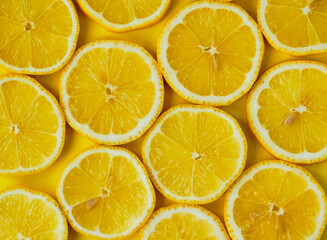 Sliced lemons in round slices on yellow background.