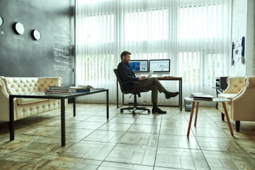 Preparing sales report. Full length of a young successful businessman sitting at his workplace in the modern office, working on laptop